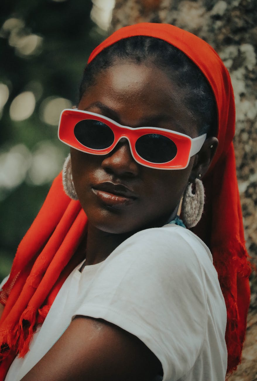 10 Accessory Mistakes Secretly Ruining Your Outfits (+ Fix) Fashionable woman with red sunglasses and scarf posing against a tree outdoors.